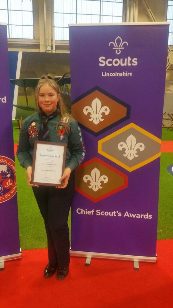Scout holding a certificate beside a Scouts award banner.