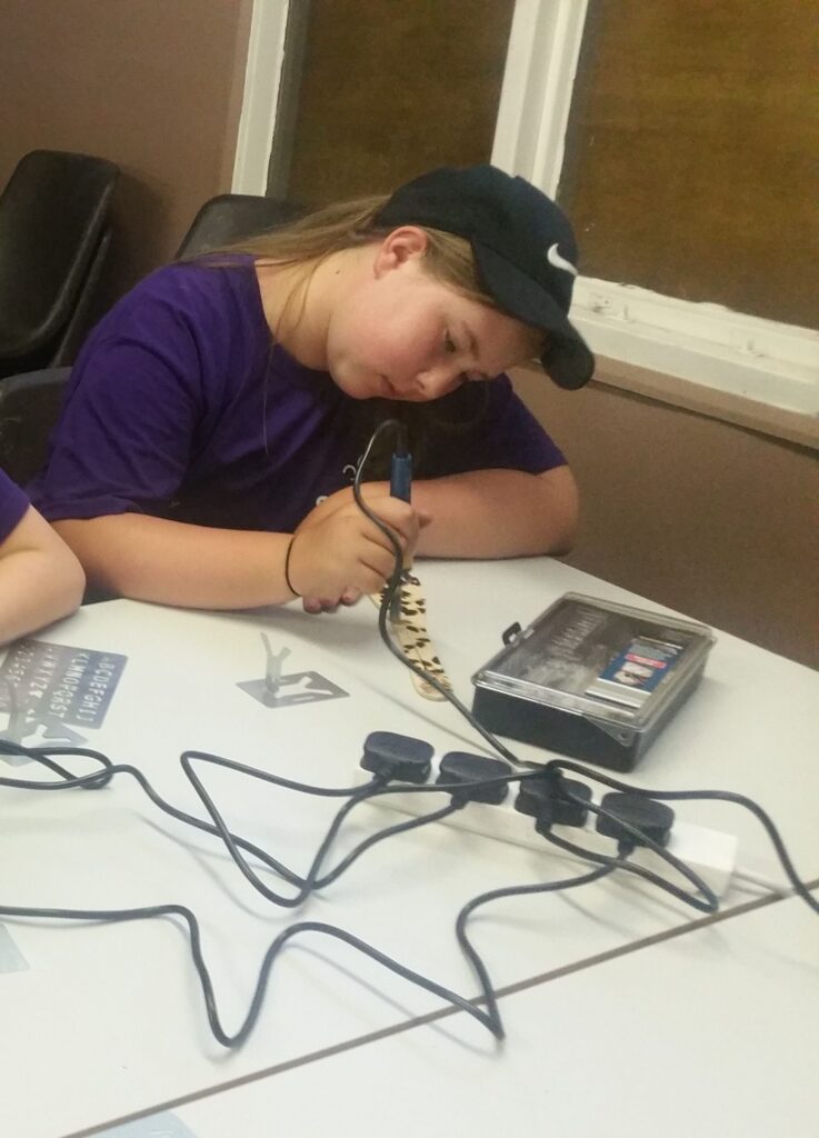Scout using a woodburning tool at a craft table.