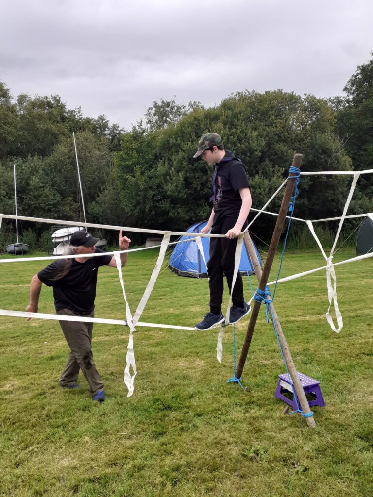 Scout crossing a rope bridge built from poles and ropes.