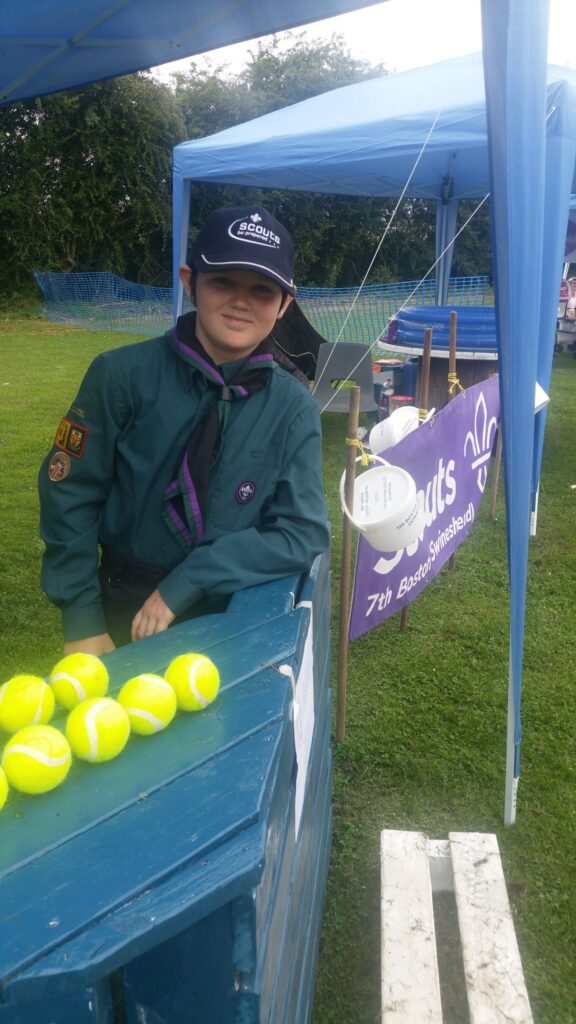 Scout in uniform beside an outdoor activity stand.