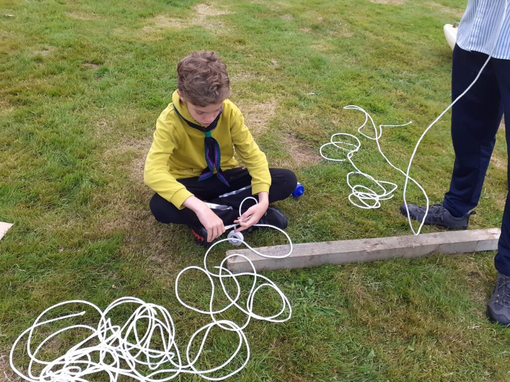 Scout practising knots with rope on the grass.