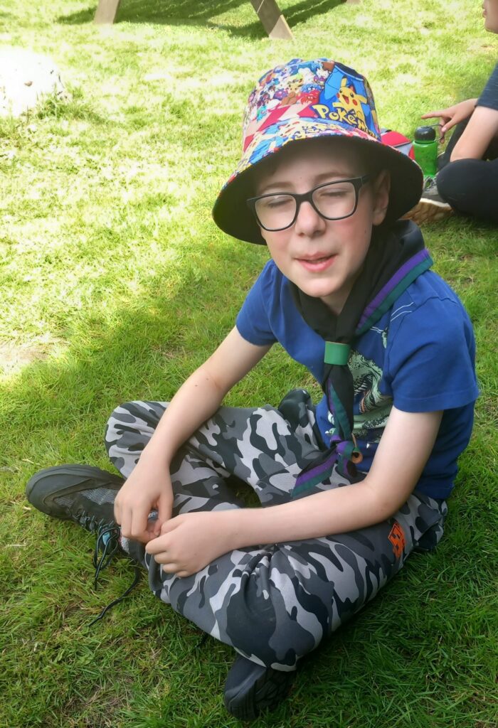 Scout wearing a sun hat sitting on the grass at camp.