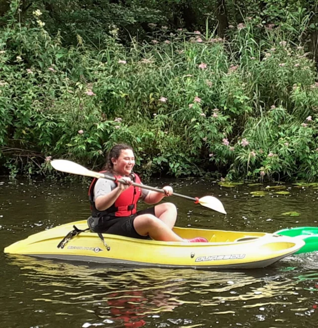 Kayaker paddling alongside a leafy riverbank.