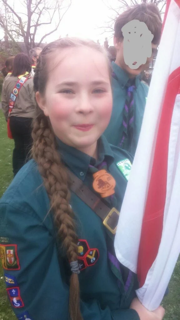 Scout in uniform standing beside a flag.